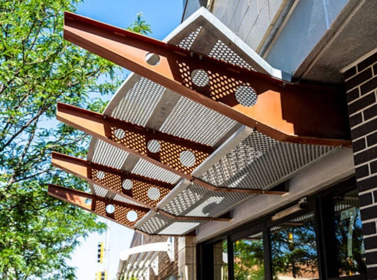 Decorative airfoil-sunshades with perforated metal panels above storefront windows.