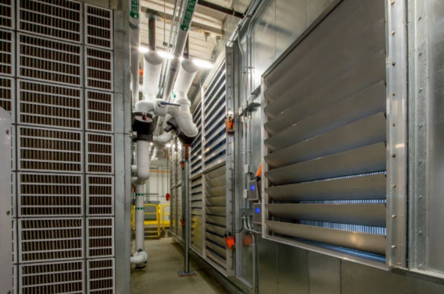 Industrial mechanical room with large metal dampers, ventilation panels, and insulated piping.